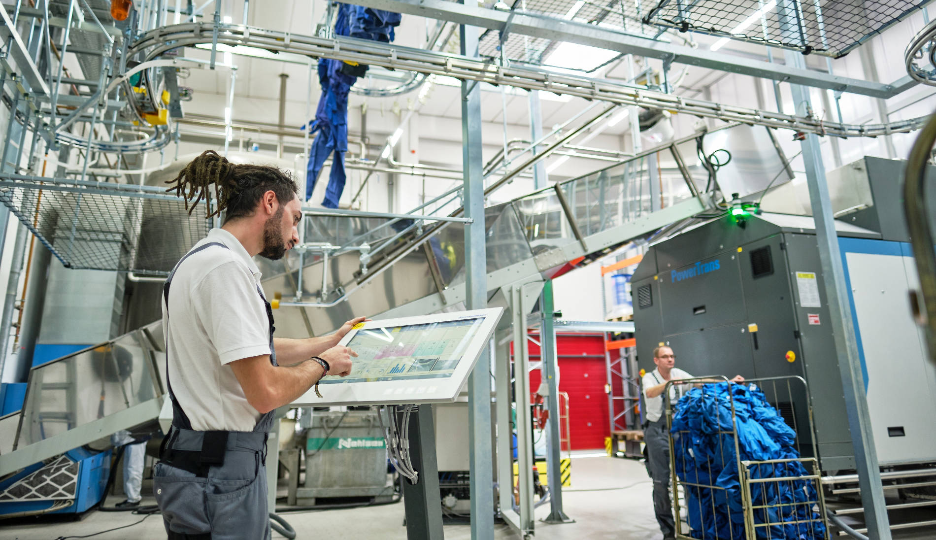 Mitarbeiter bedient in industrieller Wäscherei einen großen Touchscreen zur Steuerung moderner Textilpflegeanlagen.