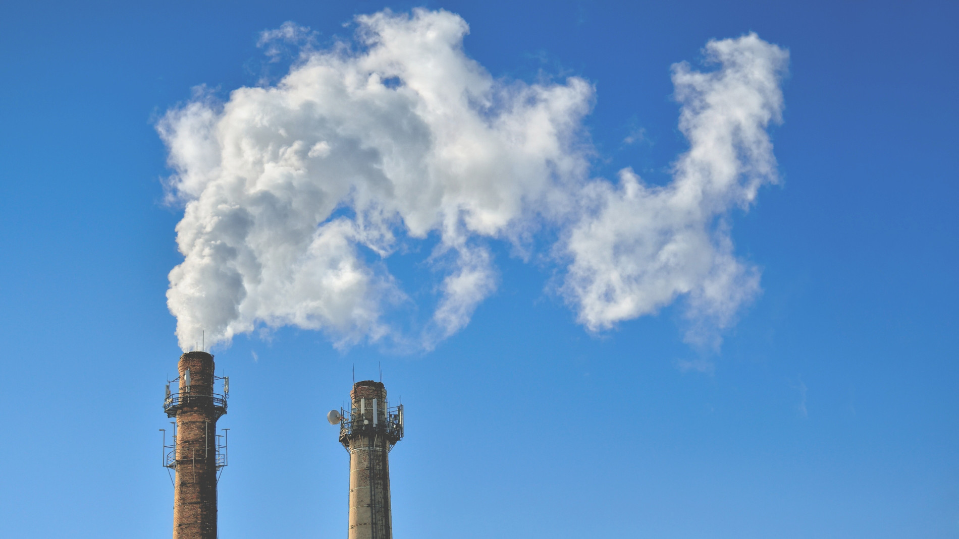 Two industrial chimneys emit smoke